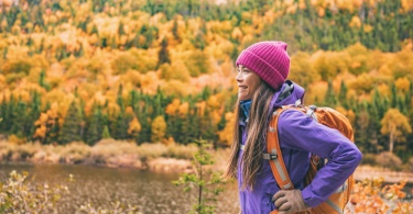 Fall autumn hiker girl outdoor at nature forest lake with backpack for camping travel trip.