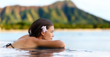 Infinity pool resort woman relaxing at sunset overlooking Waikiki beach in Honolulu city, Oahu island, Hawaii, USA. Wellness and relaxation concept for summer vacations.