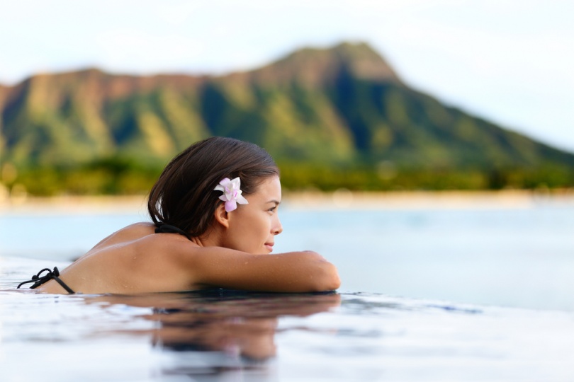 Infinity pool resort woman relaxing at sunset overlooking Waikiki beach in Honolulu city, Oahu island, Hawaii, USA. Wellness and relaxation concept for summer vacations.