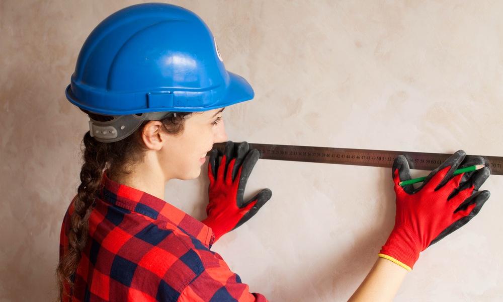 a woman with hard hat on measuring a wall