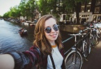 Happy young girl photographer takes selfie near canals in Amsterdam, Netherlands.