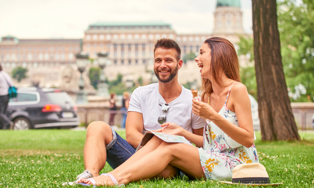 A beautiful young couple are siting in the grass having an ice-cream with the Castle in background in Budapest, Hungary.