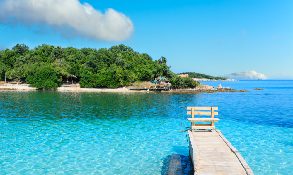 Beautiful Ionian Sea with clear turquoise water, wooden pier and morning summer coast view from beach (Ksamil, Albania)