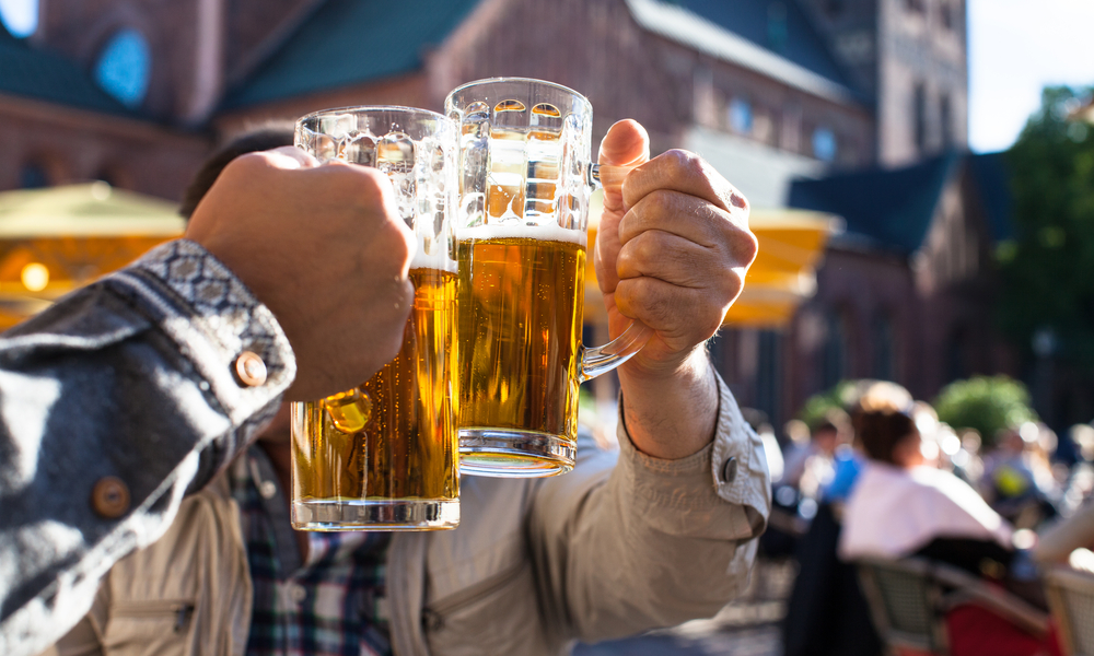 Happy male friends drinking beer and clinking glasses at bar. Europe