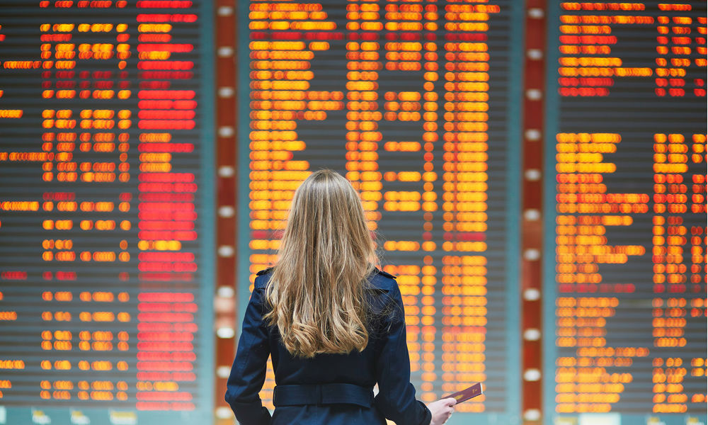 an airport screen shows flight s being canceled while a woman looks on