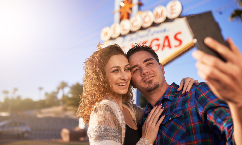 romantic couple taking selfie by welcome to las vegas sign with smart phone