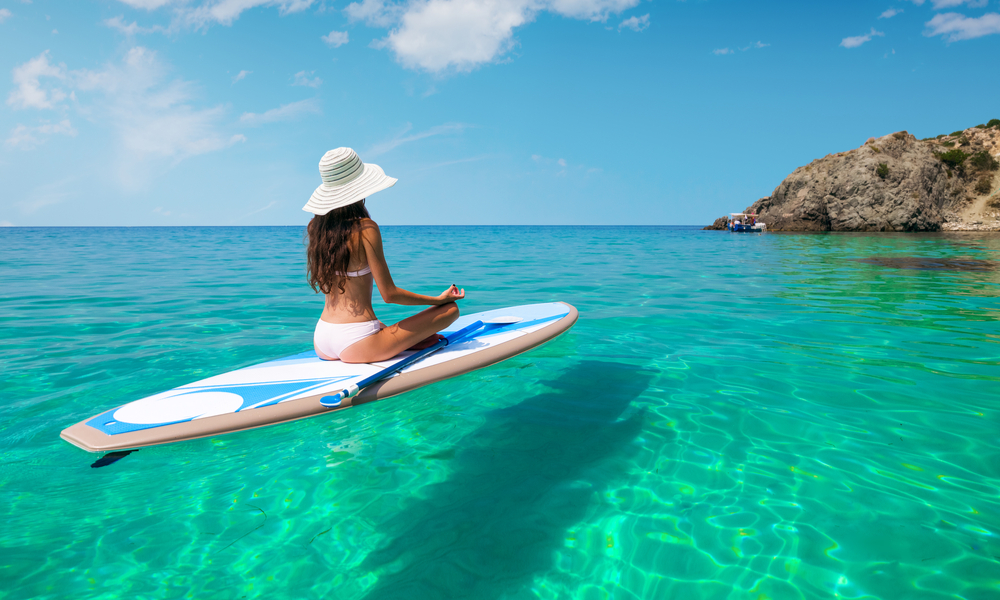 A beautiful young woman relaxes on a SUP board in the sea near the island. Standup paddleboarding on Hawaii.