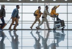 Full length profile of joyful young friends are running along terminal hall with suitcases.