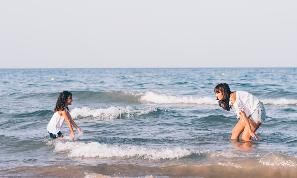 Pretty woman with short blue jeans and her daughter playing in the beach water.