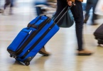 Woman walking quickly pulling blue luggage in busy airport