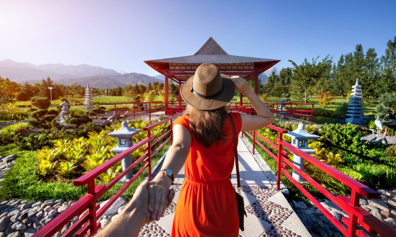 Woman in orange dress and hat holding man by hand going to Japanese Garden with pagoda