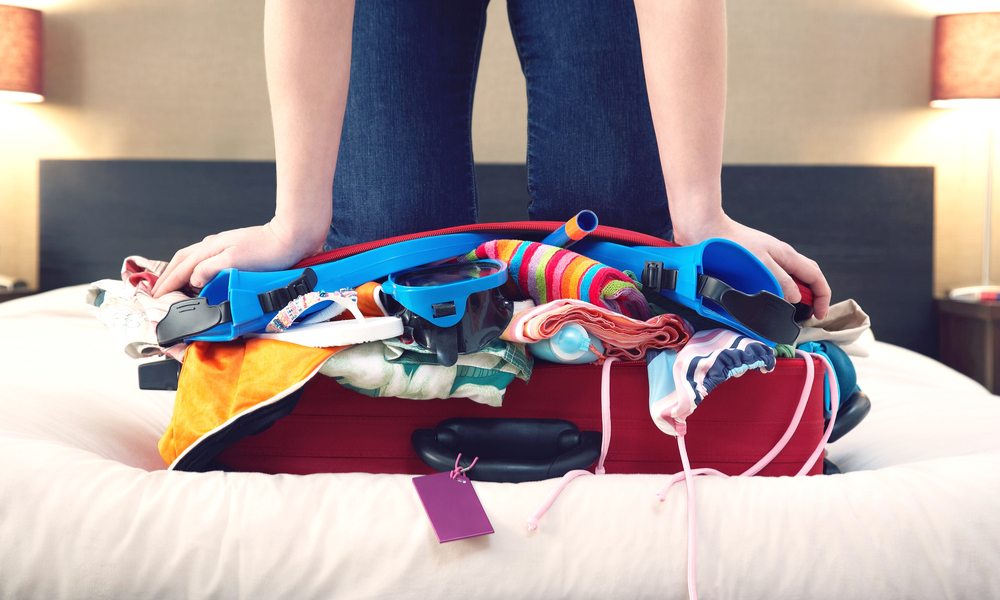 woman kneeling on overstuffed suitcase in bed