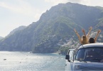 Beautiful happy tourist girl friends enjoying scenic view arms raised of Amalfi Coast on summer road trip adventure vacation in vintage van