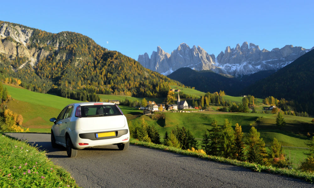 Road trip in a white car in autumn through the Funes valley in Dolomites area in South Tyrol, Italy with the village of Sankt Magdalena in the background.