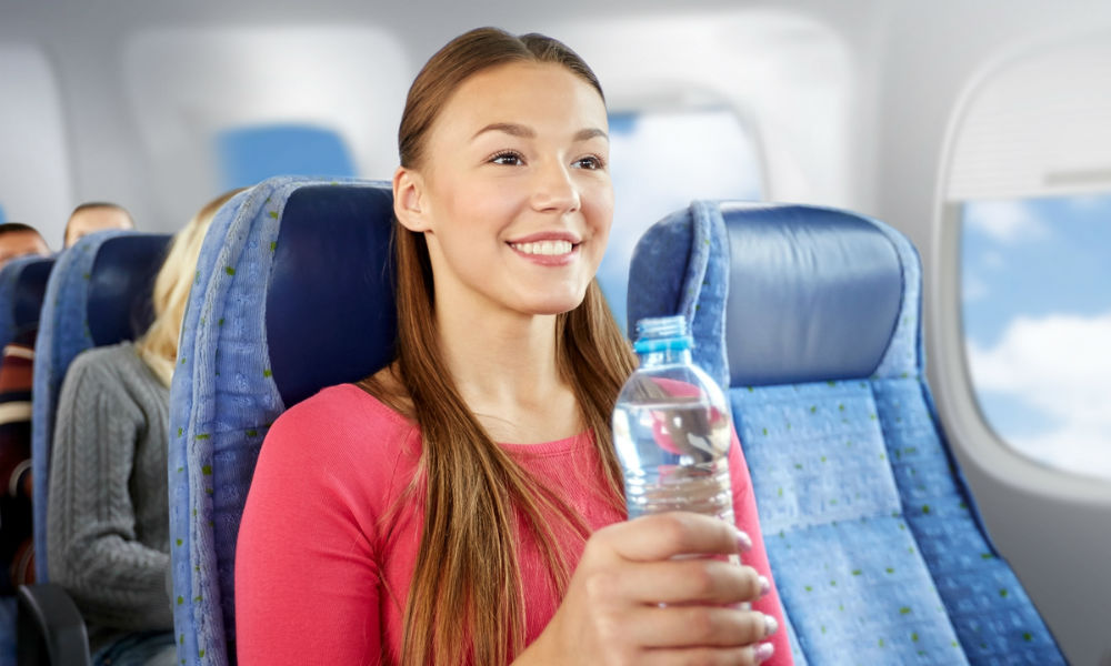 happy young woman with water bottle in plane over porthole background