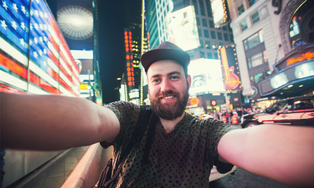 bearded man backpacker smiling and taking selfie photo on Times Square in New York 