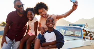 family taking a selfie leaning on a car