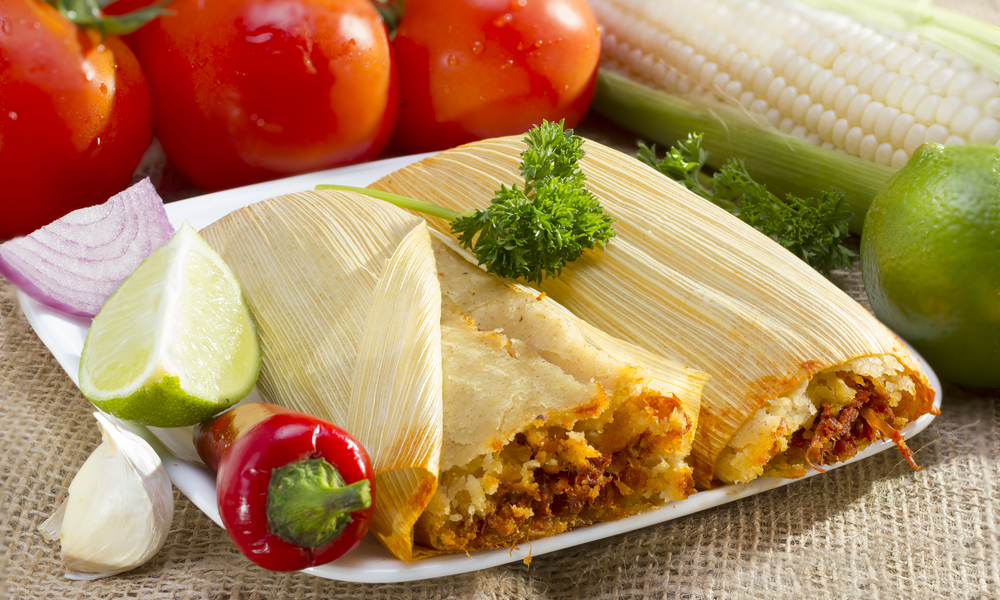 Mexican tamale wrapped in corn husk served on plate.