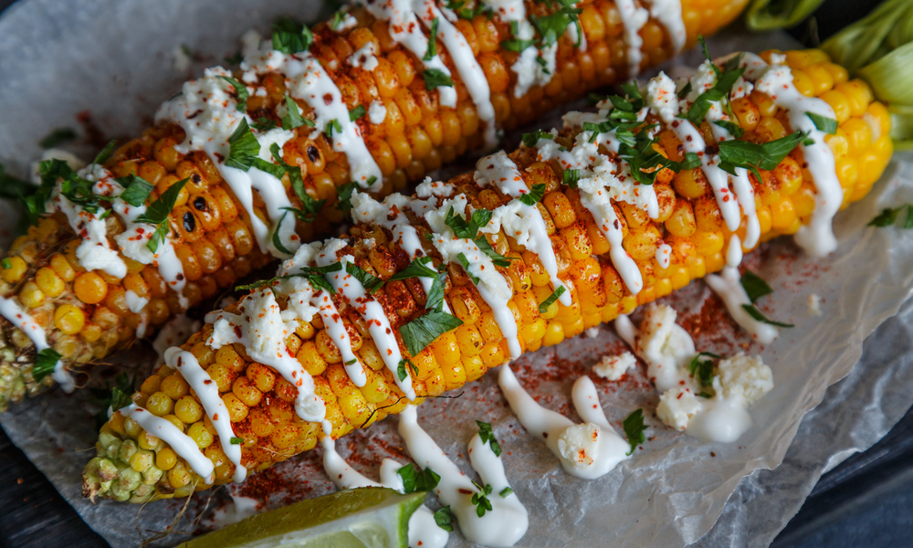 Grilled corn cobs on wooden plate, mexican style, close view.