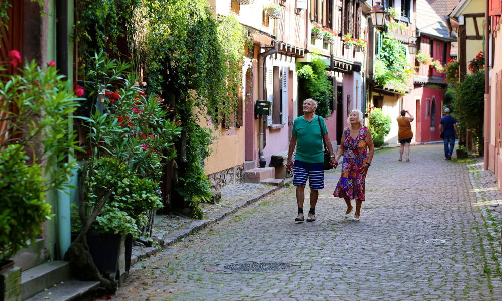 Elderly couple visiting Alsace region, walking on the streets of Kaysersberg town.