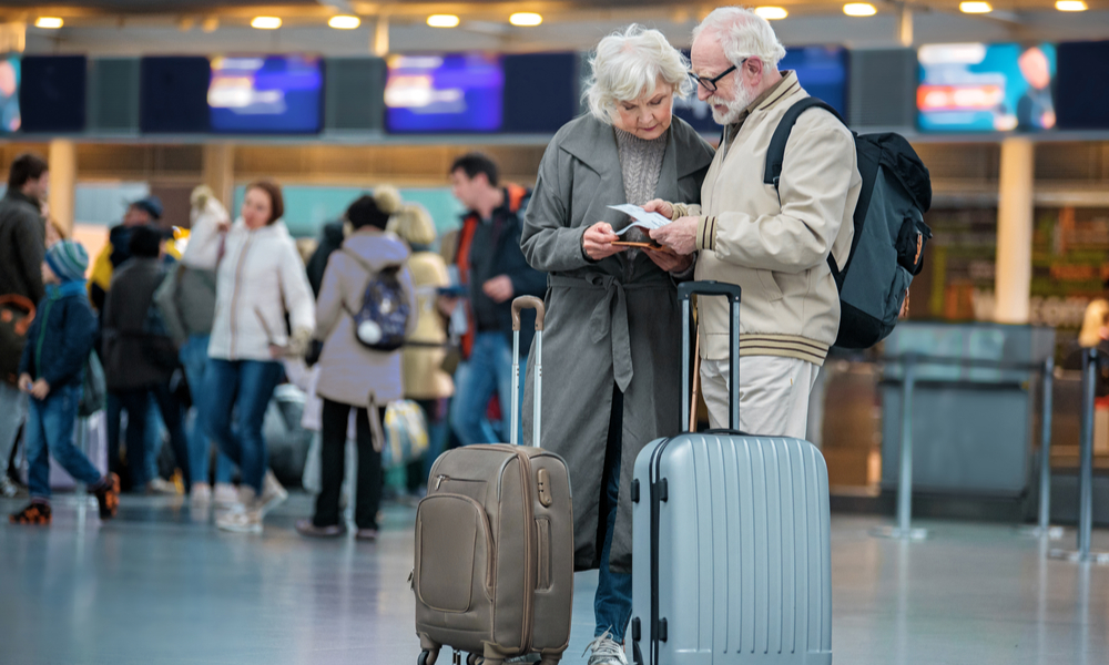 senior wife and husband are standing with suitcases at international airport and looking at flight tickets 