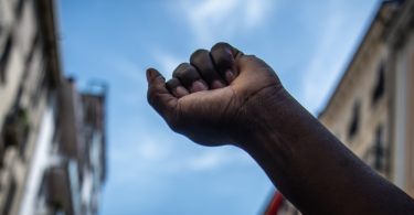 A black man raises his fist to the sky during a migrants protest against racial discrimation. B