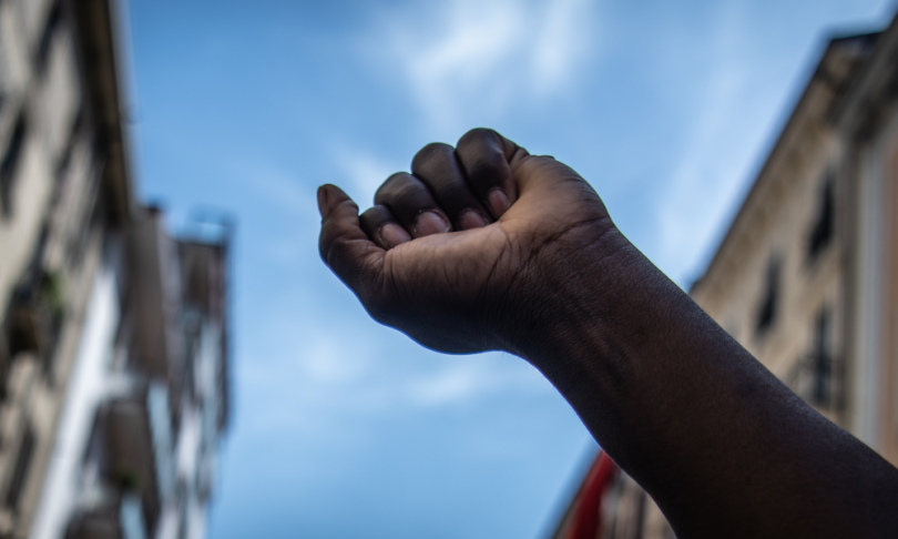 A black man raises his fist to the sky during a migrants protest against racial discrimation. B