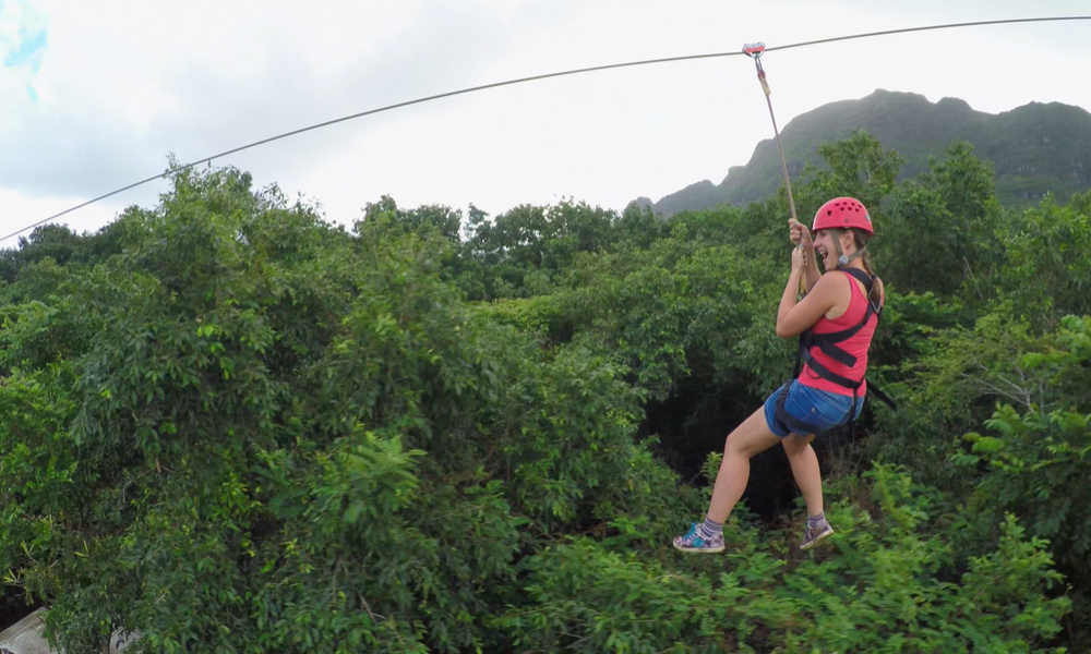 Young happy woman sliding on high speed zipline rope above beautiful tropic deciduous forest. 