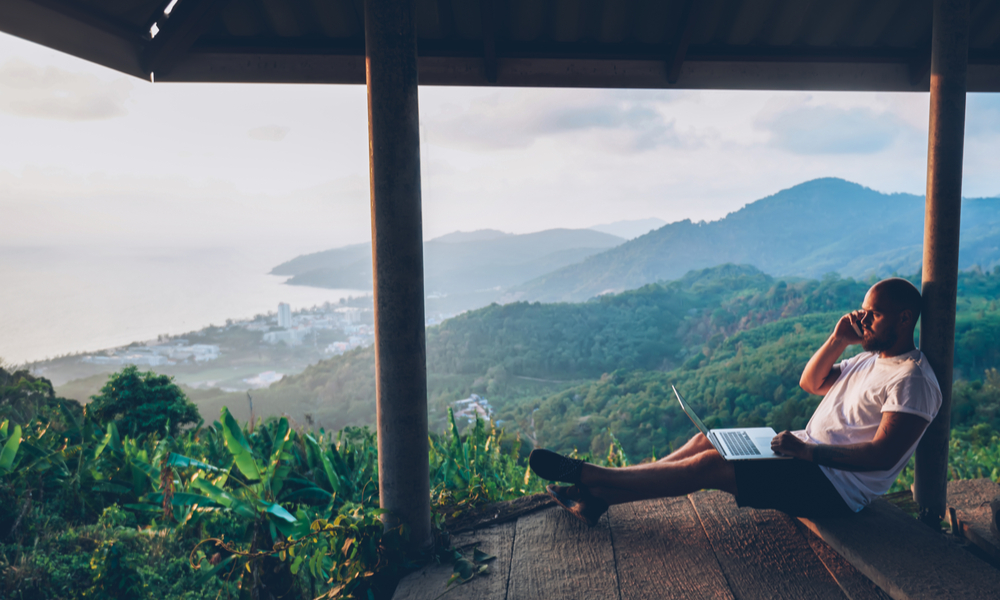 Male freelancer using internet connection and modern devices outdoors against tropical environment 