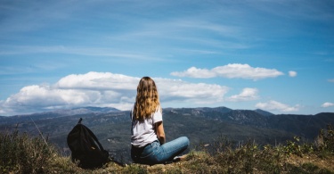 Woman traveler hipster with a backpack seating on the top of mountain with incredible amazing view on the valley