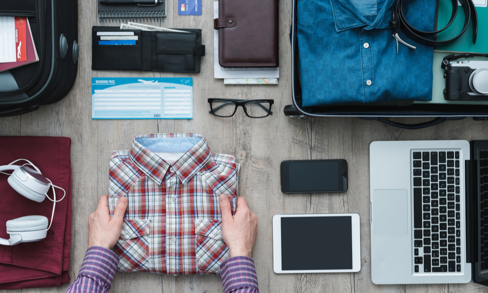 Getting ready for a trip and packing a suitcase, a man is holding his shirt before putting it into his bag, travel and vacations concept