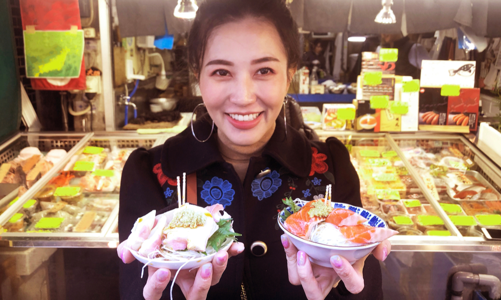  The Tokyo Food Scene: Were to Go & What to Eat: woman showing salmon sashimi most popular delicious food in street food tsukiji fish market, Japan