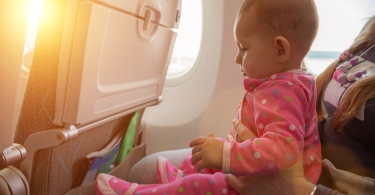 How to prepare for flying with a toddler for the first time: Mother and baby sitting together in airplane near the window in sunny day