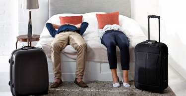 Simple Ways to Deal with Jet Lag on International Flights: Indoor shot of mature couple lying on bed with luggage