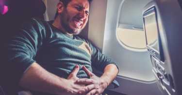 Foods to avoid when flying: man with stomach ache on passenger flight